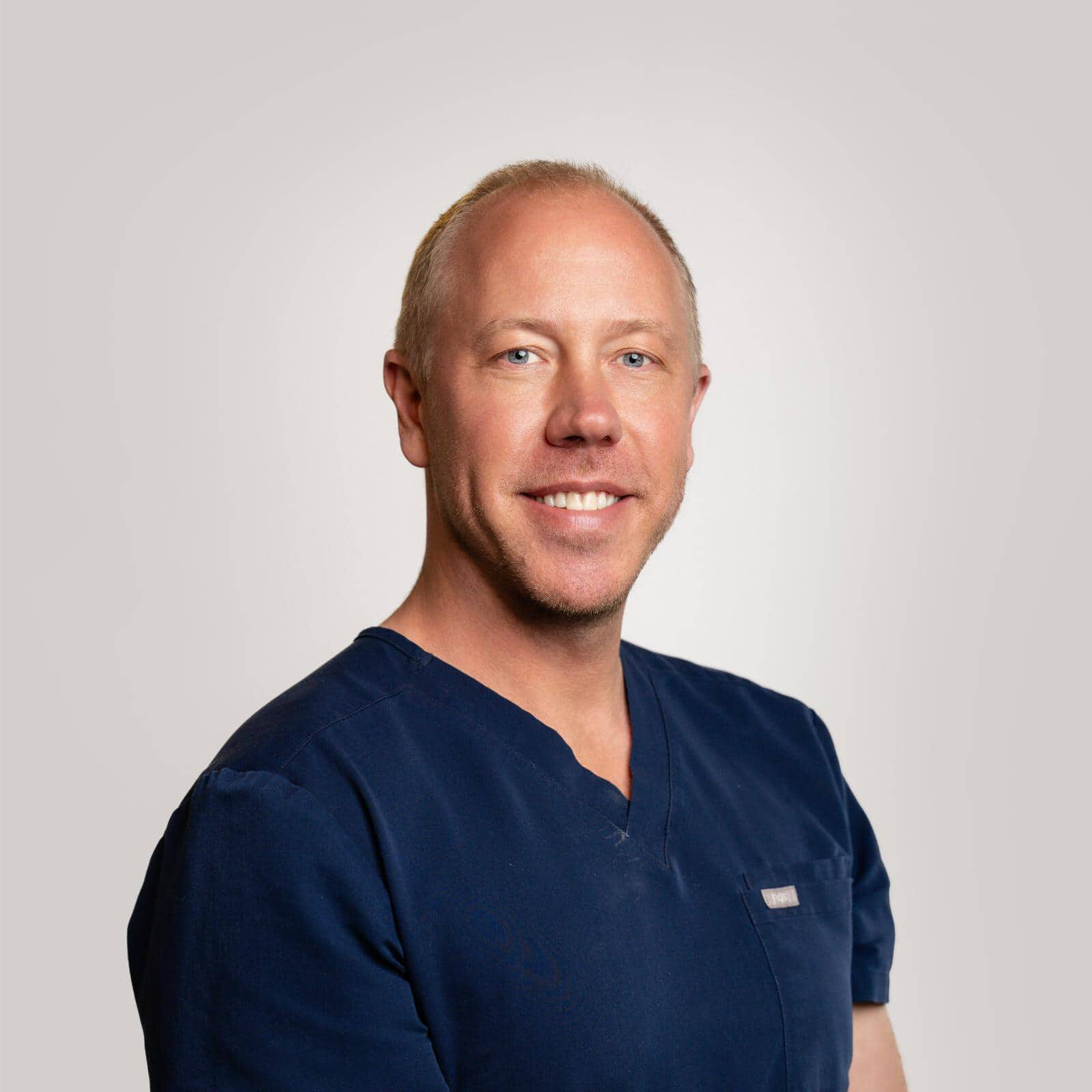 Dr. Ross Pulver, board-certified orthodontist in navy scrubs, smiling against a neutral background, representing North County Orthodontics.